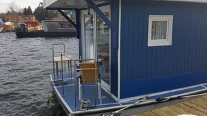 Una estructura azul flotante con una pequeña terraza, una silla y un ventanal.