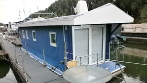 Una cabaña azul con una mesa de vidrio y dos sillas de mimbre en un barco amarrado en un puerto deportivo.