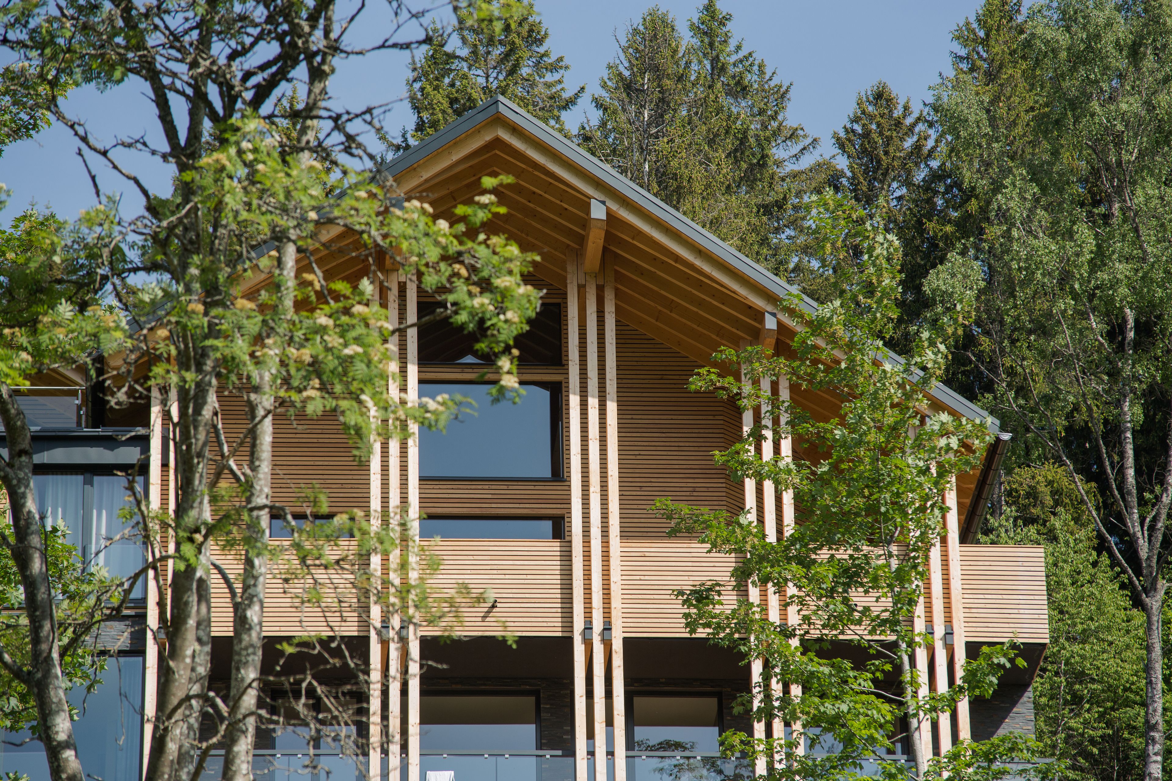 A modern multi-story building with a wooden facade, large windows, and a sloped roof.