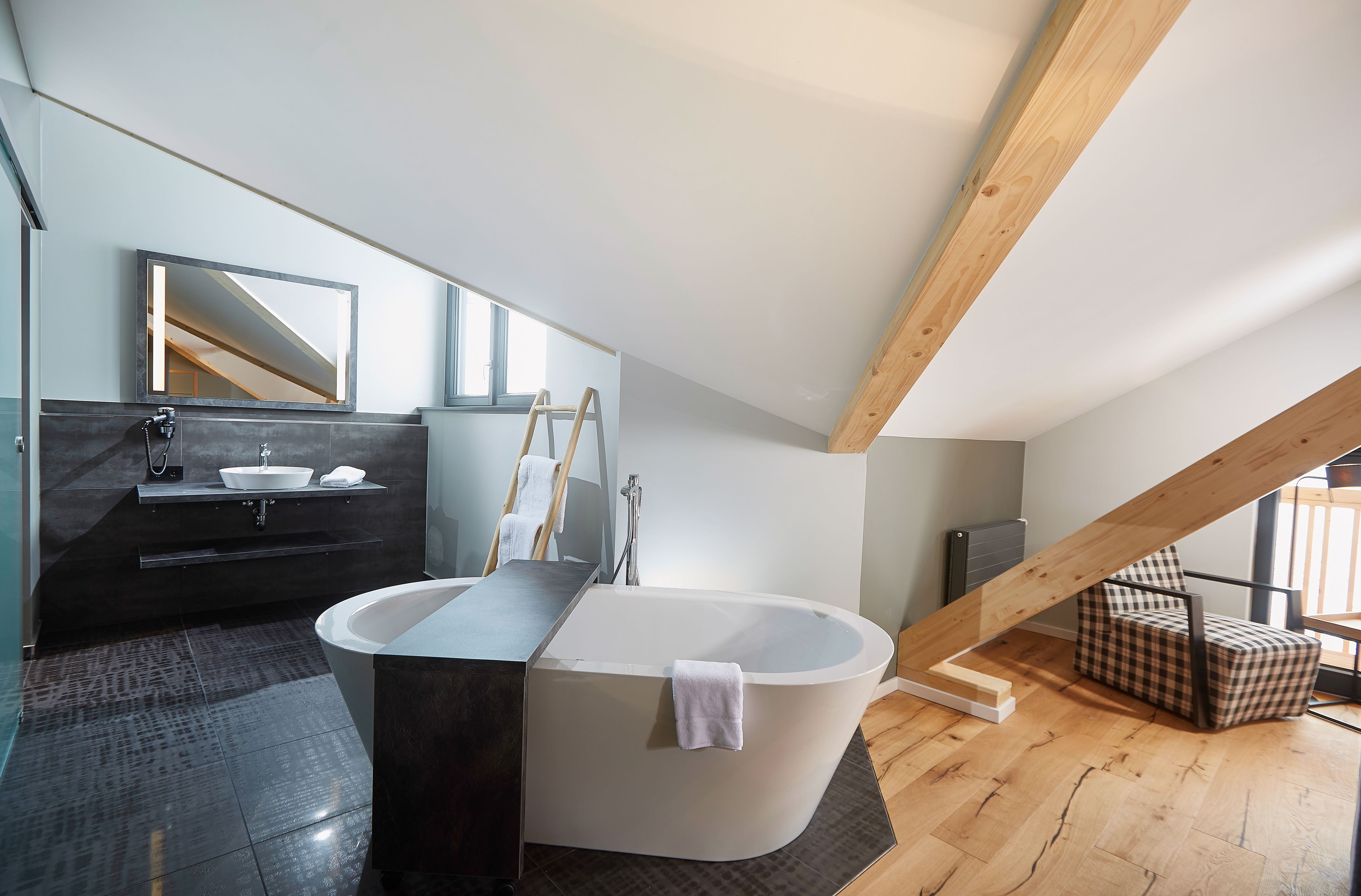 A modern bathroom with a freestanding bathtub, a vanity with a mirror, and a checkered chair.