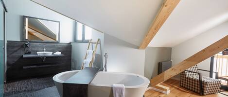 A modern bathroom with a freestanding bathtub, a vanity with a mirror, and a checkered chair.