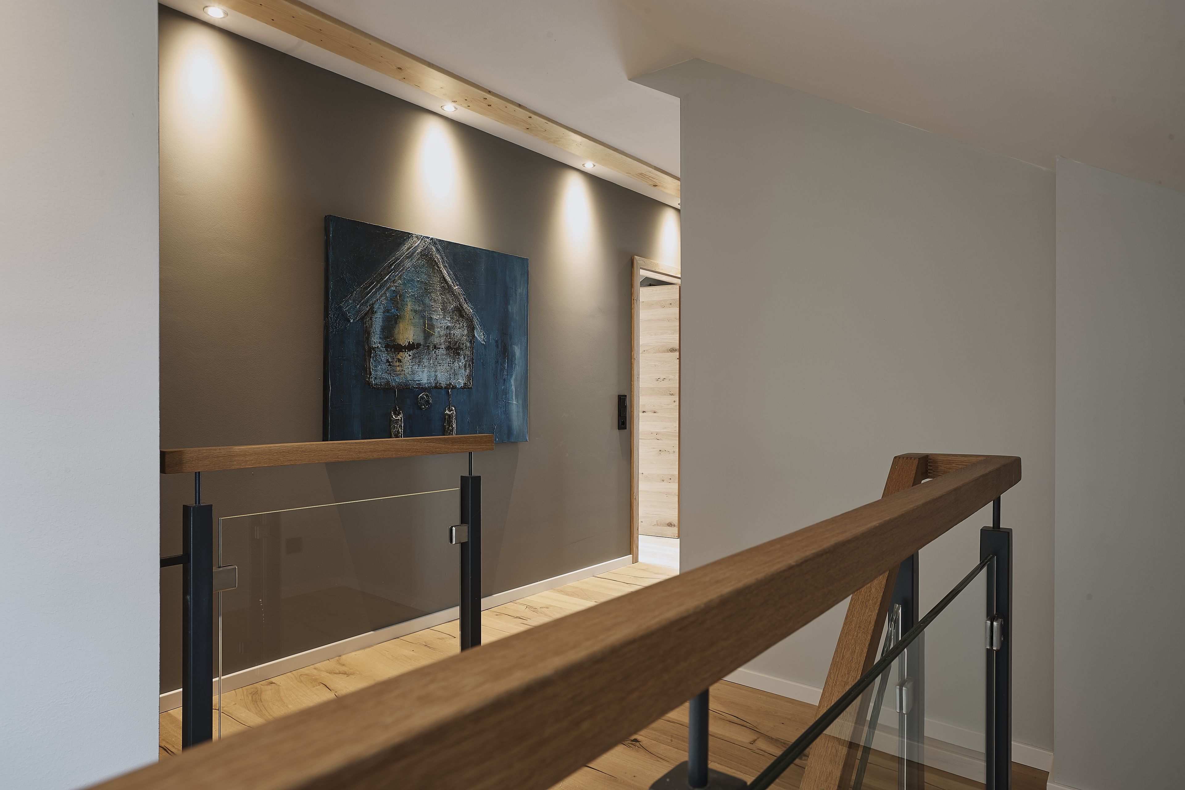 Una escalera moderna con barandillas de vidrio y peldaños de madera que conduce a una habitación con un cuadro abstracto grande en la pared.