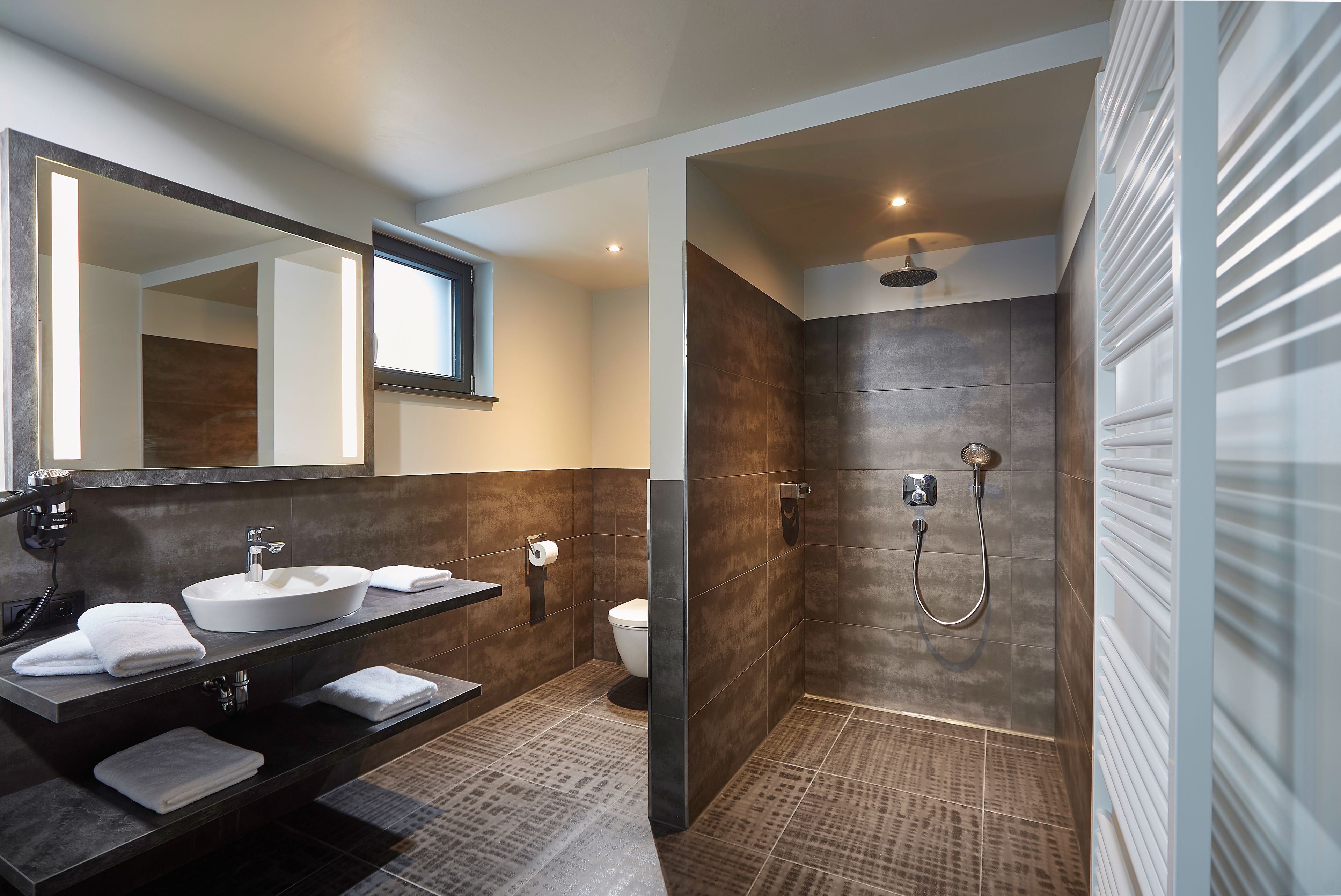A modern bathroom with a double sink vanity, a toilet, and a walk-in shower with a glass door.