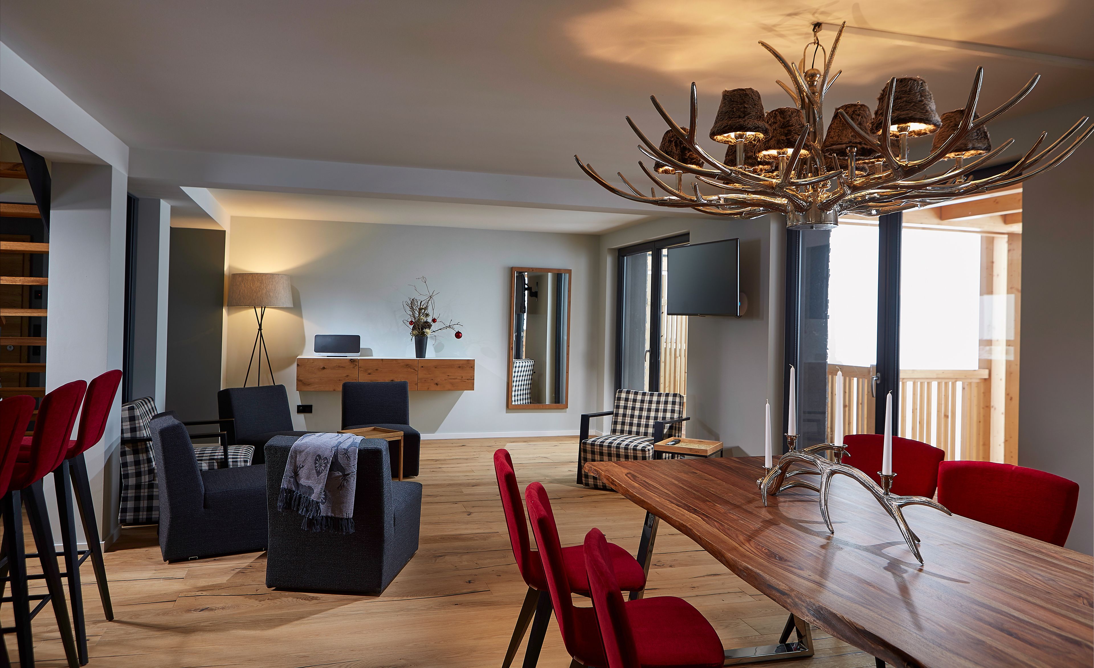 A modern dining area with a wooden table, red chairs, and a unique chandelier.
