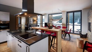 A modern kitchen with a central island, a dining area with red chairs, and large windows offering a view of a snowy landscape. - Black Forest Lodge (Feldberg)