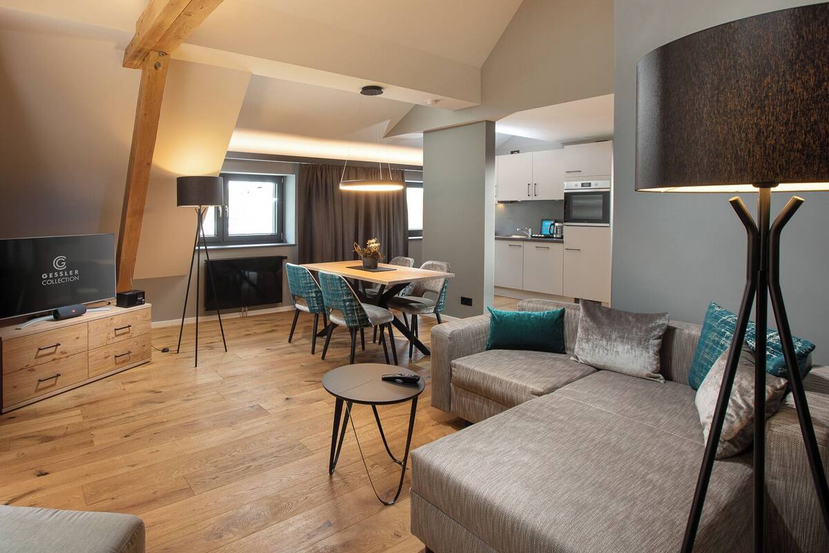 A modern living room with a sofa, a coffee table, a TV, and a dining area with chairs and a table.
