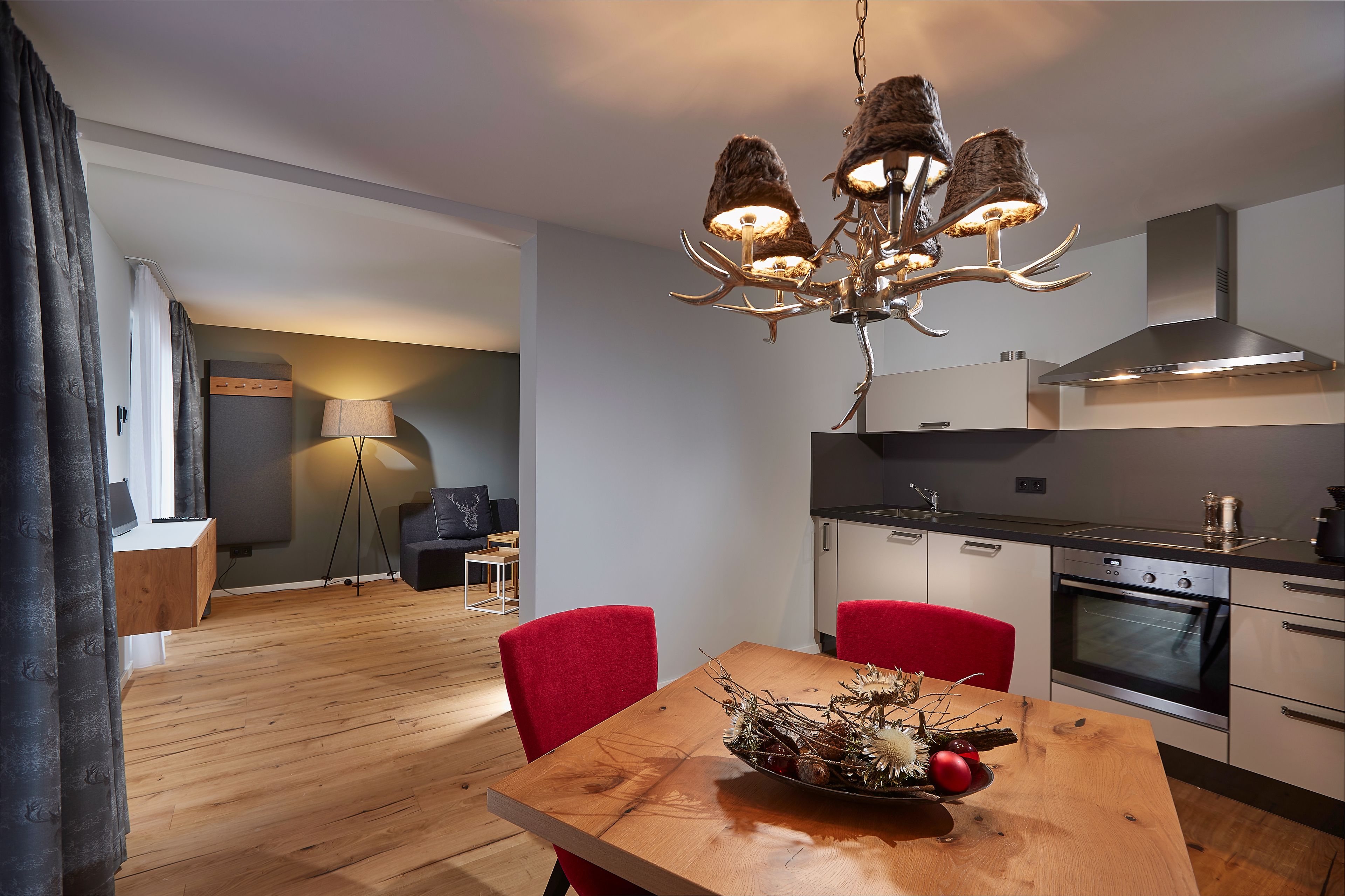 A modern kitchen with a wooden dining table, red chairs, and a chandelier.