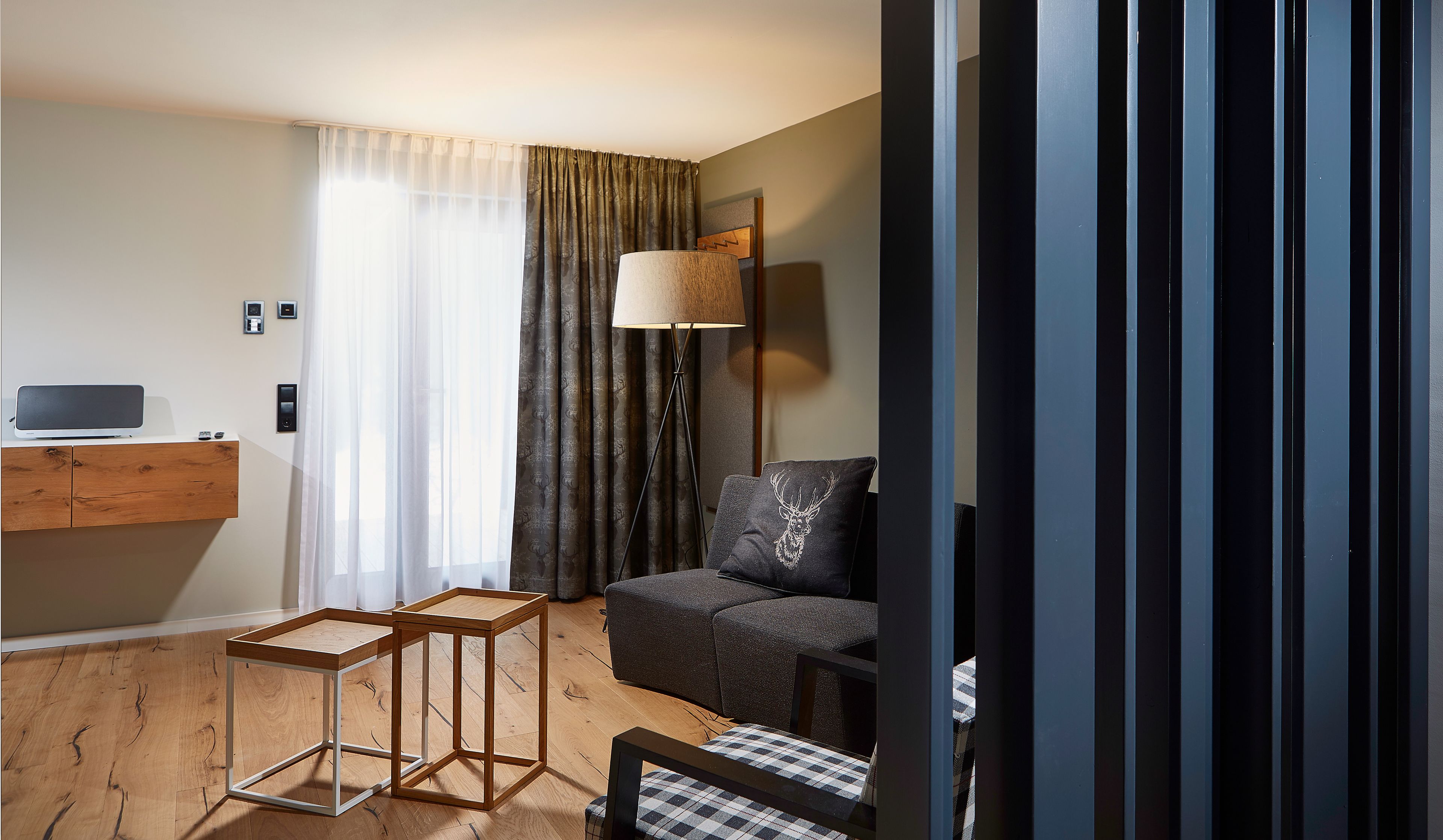 A modern hotel room with a wooden desk, a sofa, a lamp, and a view of the outdoors.