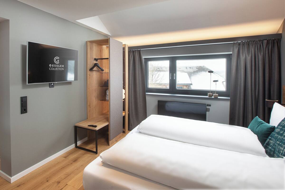 A modern hotel room with a bed, a TV, a desk, and a wardrobe.