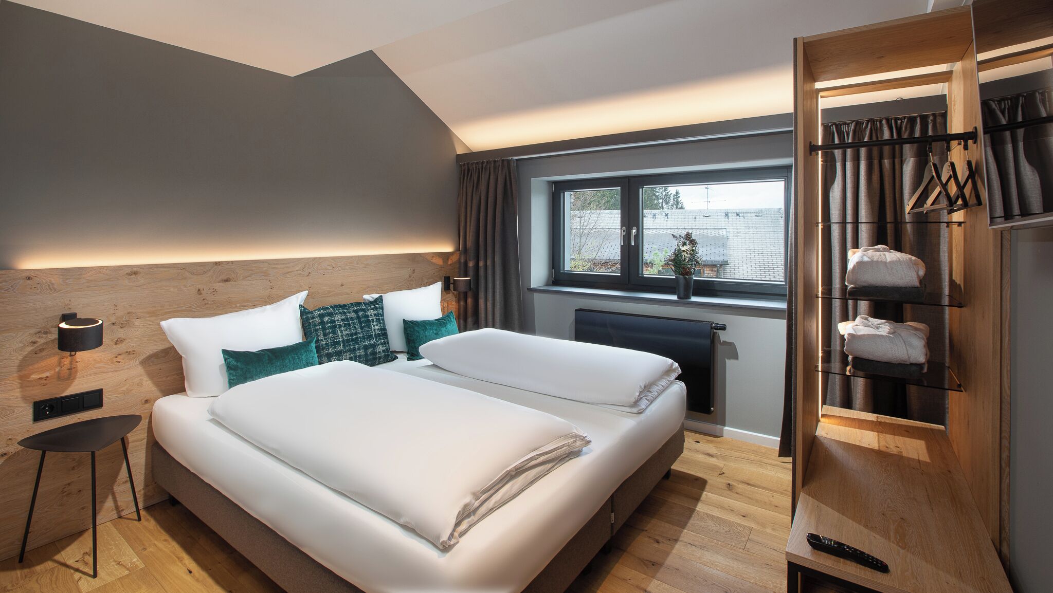 A modern bedroom with a large bed, a bedside table, a nightstand, a window with curtains, and a built-in wardrobe with shelves.