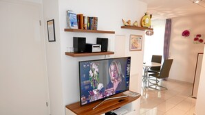 A modern living room with a flat-screen TV, wooden entertainment unit, bookshelves, and a dining area with chairs. - Ferienwohnung im Atelierhaus (Meersburg)