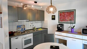 A modern kitchen with grey cabinets, a dishwasher, an oven, a coffee machine, and a dining table with a single chair. - Ferienwohnung im Atelierhaus (Meersburg)