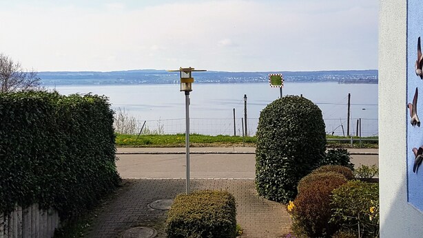 A paved walkway with a lamp post and trimmed bushes, leading to a view of a body of water and distant land. - Ferienwohnung im Atelierhaus (Meersburg)
