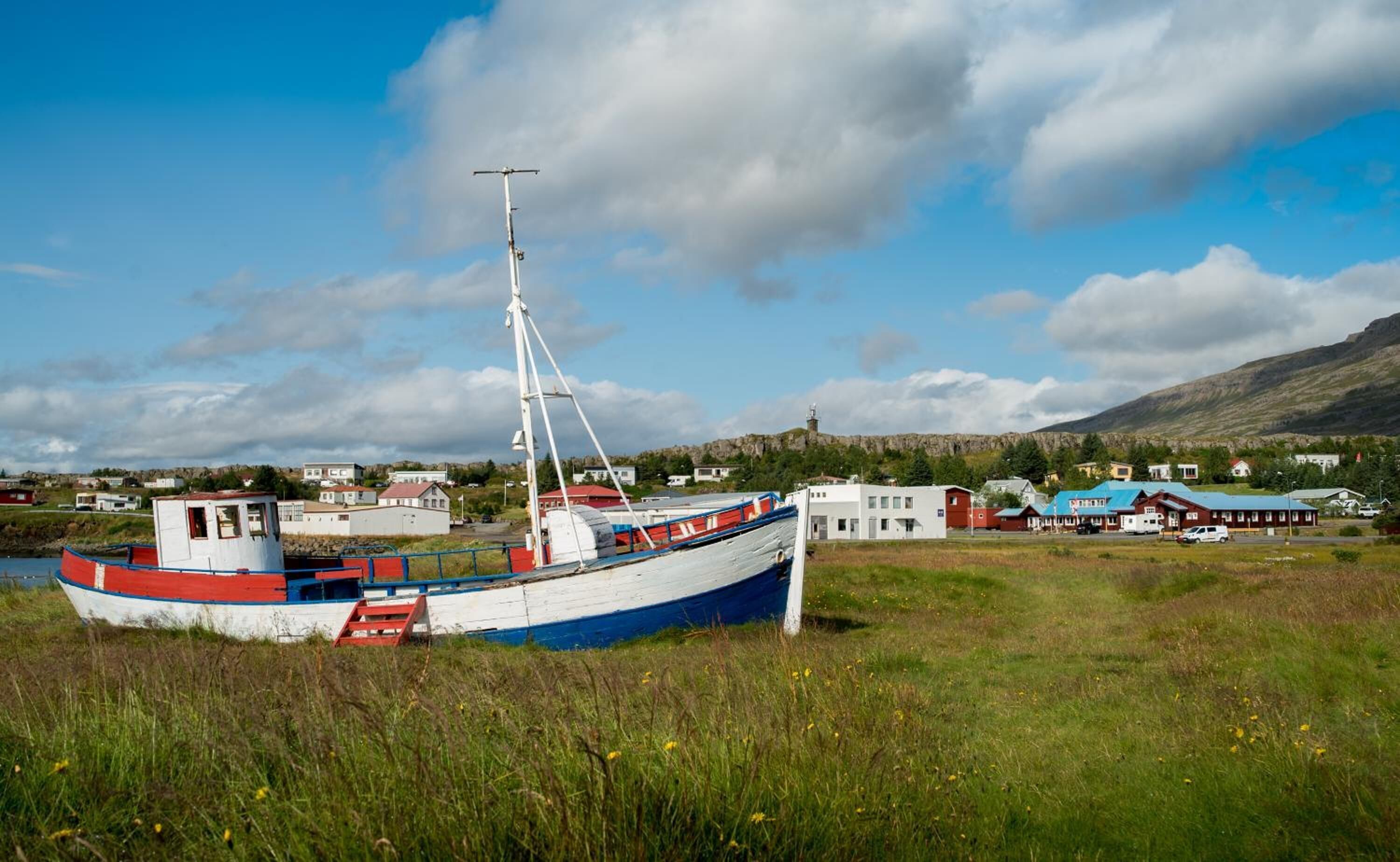 A boat docked in a grassy area with a town in the background.