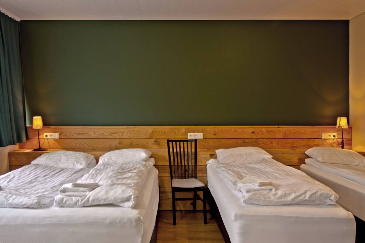 A hotel room with two single beds, a wooden headboard, a chair, and two bedside lamps.