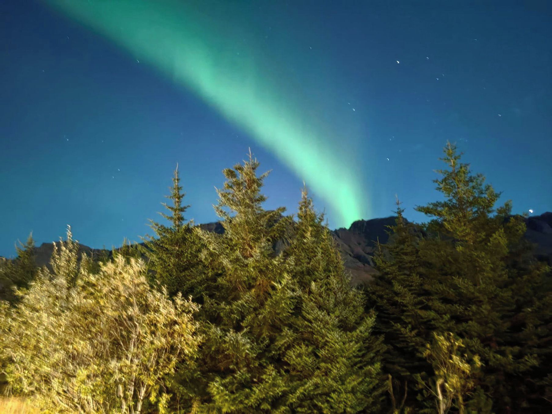 A night sky with the aurora borealis over a forested mountain range.