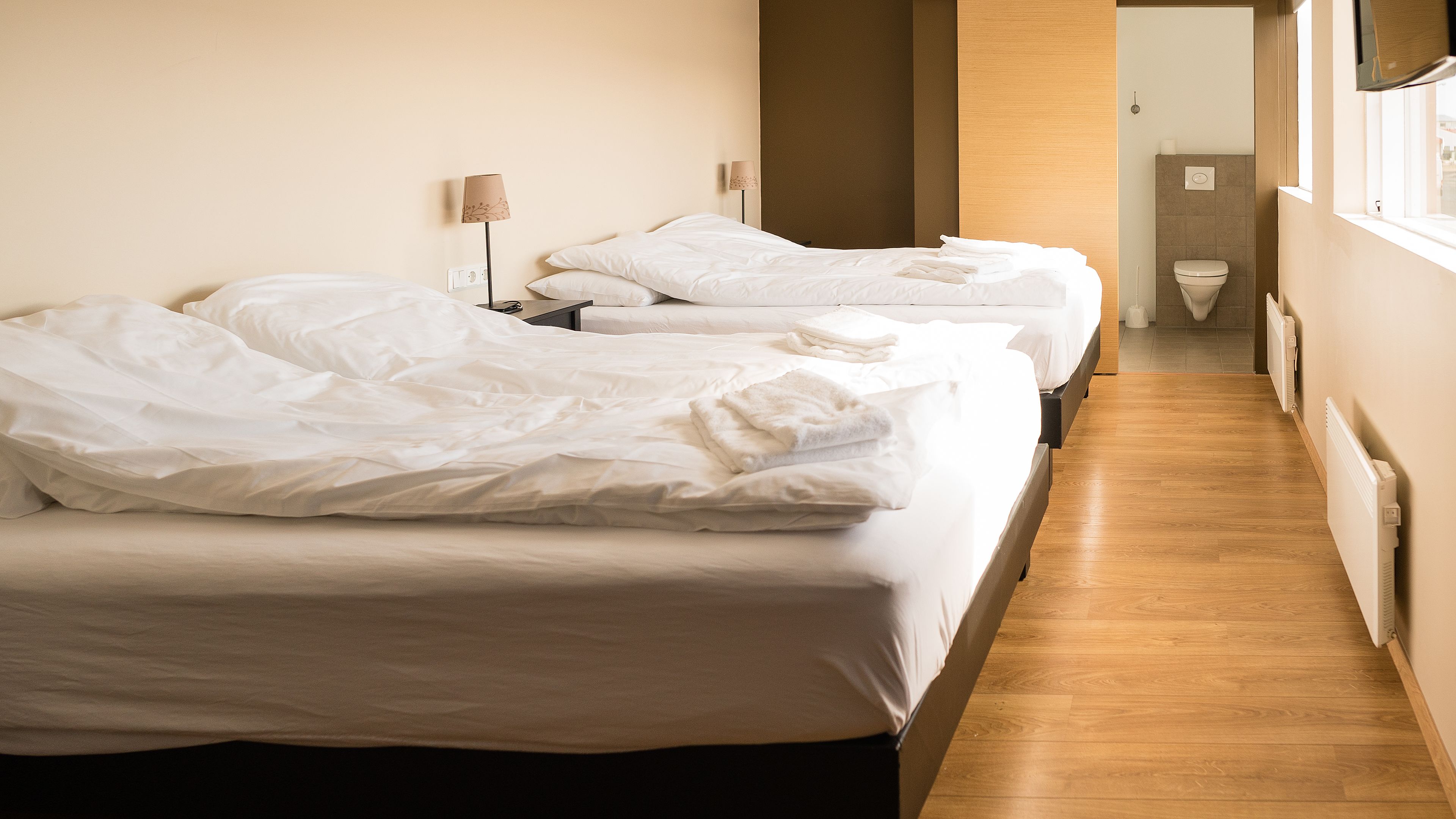 Habitación de hotel con dos camas, piso de madera y vista al pasillo.