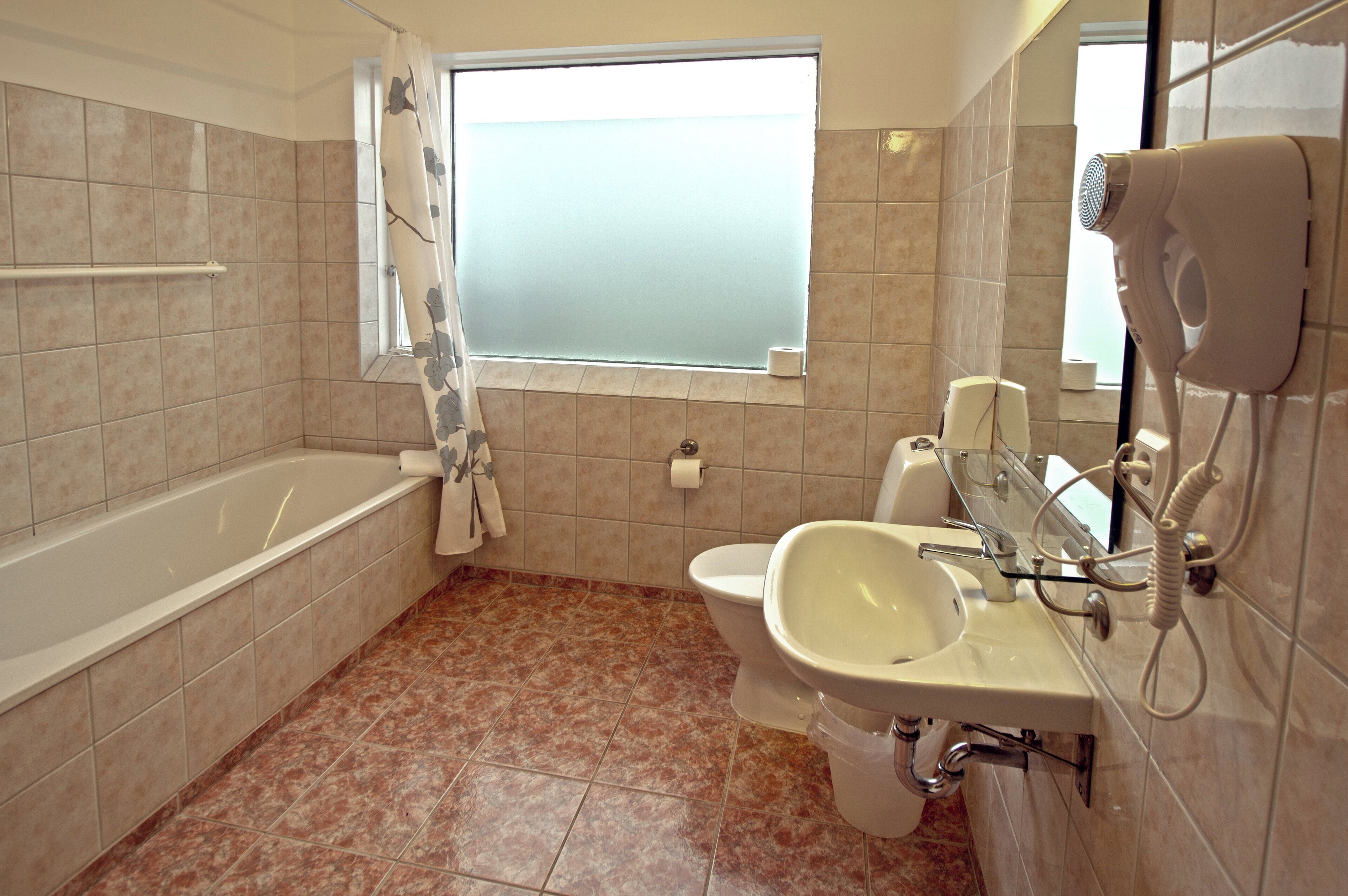 Une salle de bain équipée d’une baignoire, de toilettes, d’un lavabo et d’un sèche-cheveux fixé au mur.