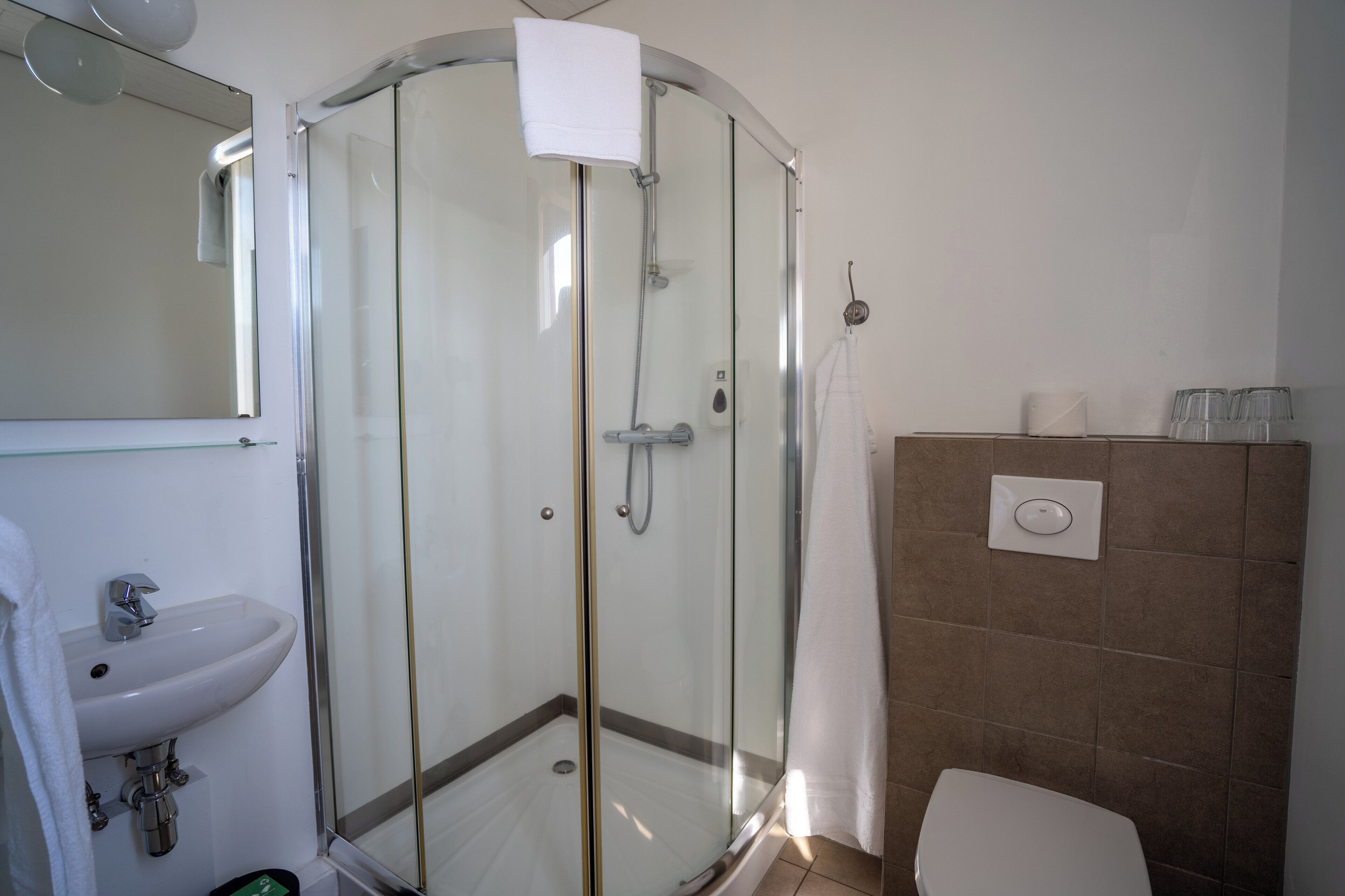 Un baño moderno con ducha de vidrio, lavamanos blanco y un inodoro.