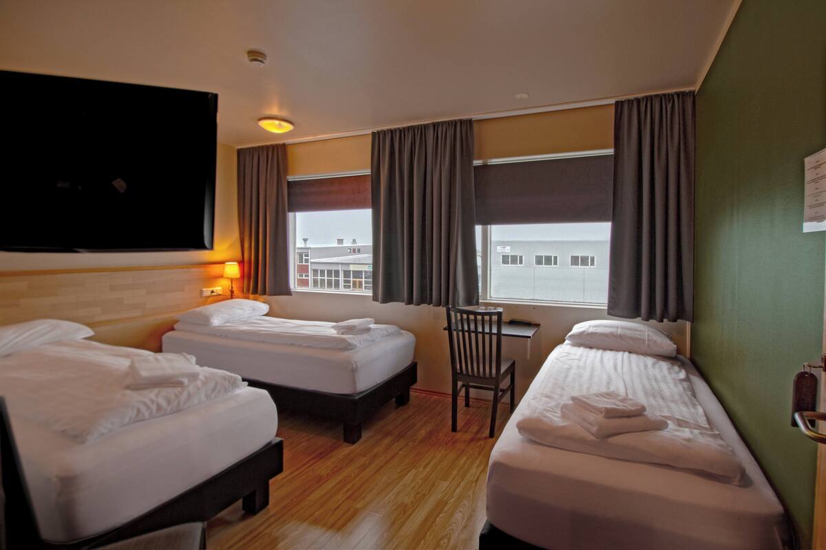 A hotel room with two single beds, a desk, a chair, a TV, and a window with curtains.