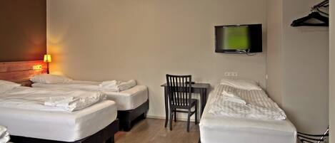 Habitación de hotel con tres camas, un escritorio, una silla, un televisor y un perchero.