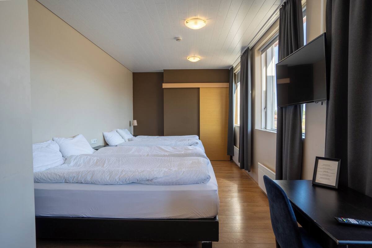 A hotel room with two beds, a desk, and a TV.