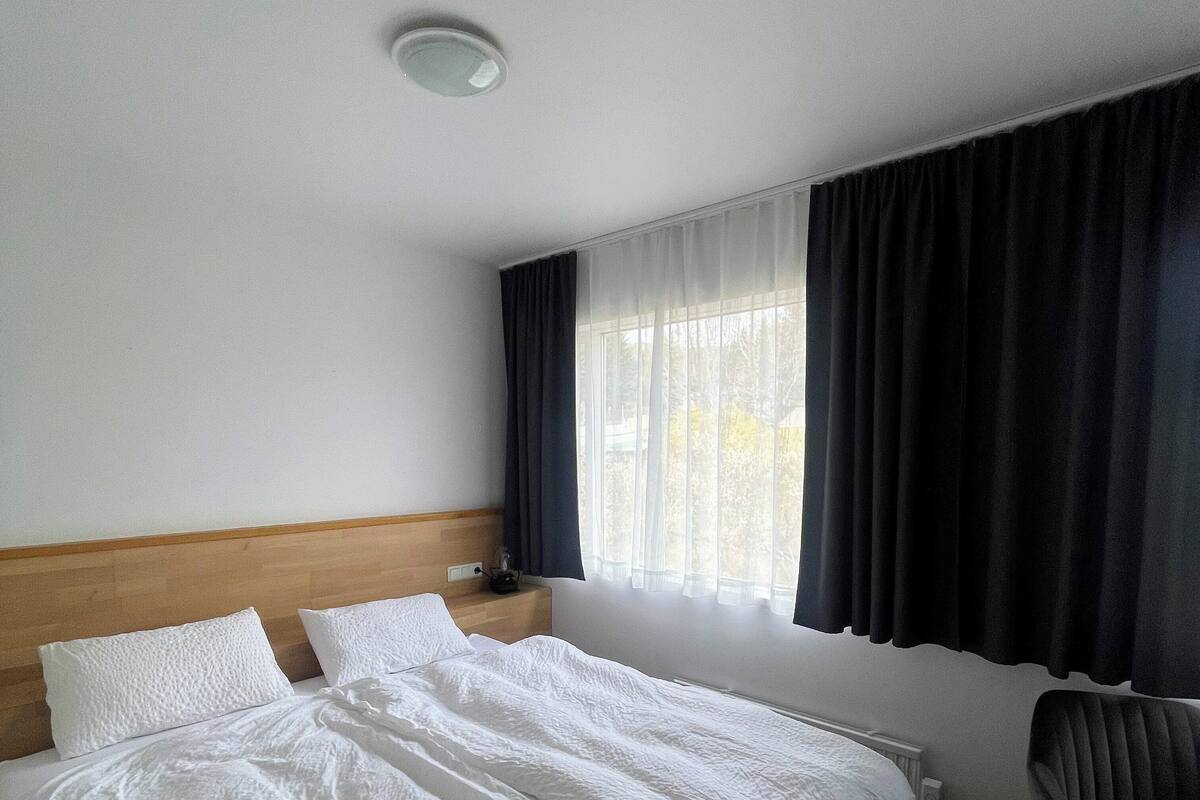 A hotel room with a large bed, a chair, a nightstand, and a window with curtains.