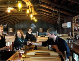 Un bar rústico con vigas de madera, lámparas colgantes y una variedad de botellas en estanterías.
