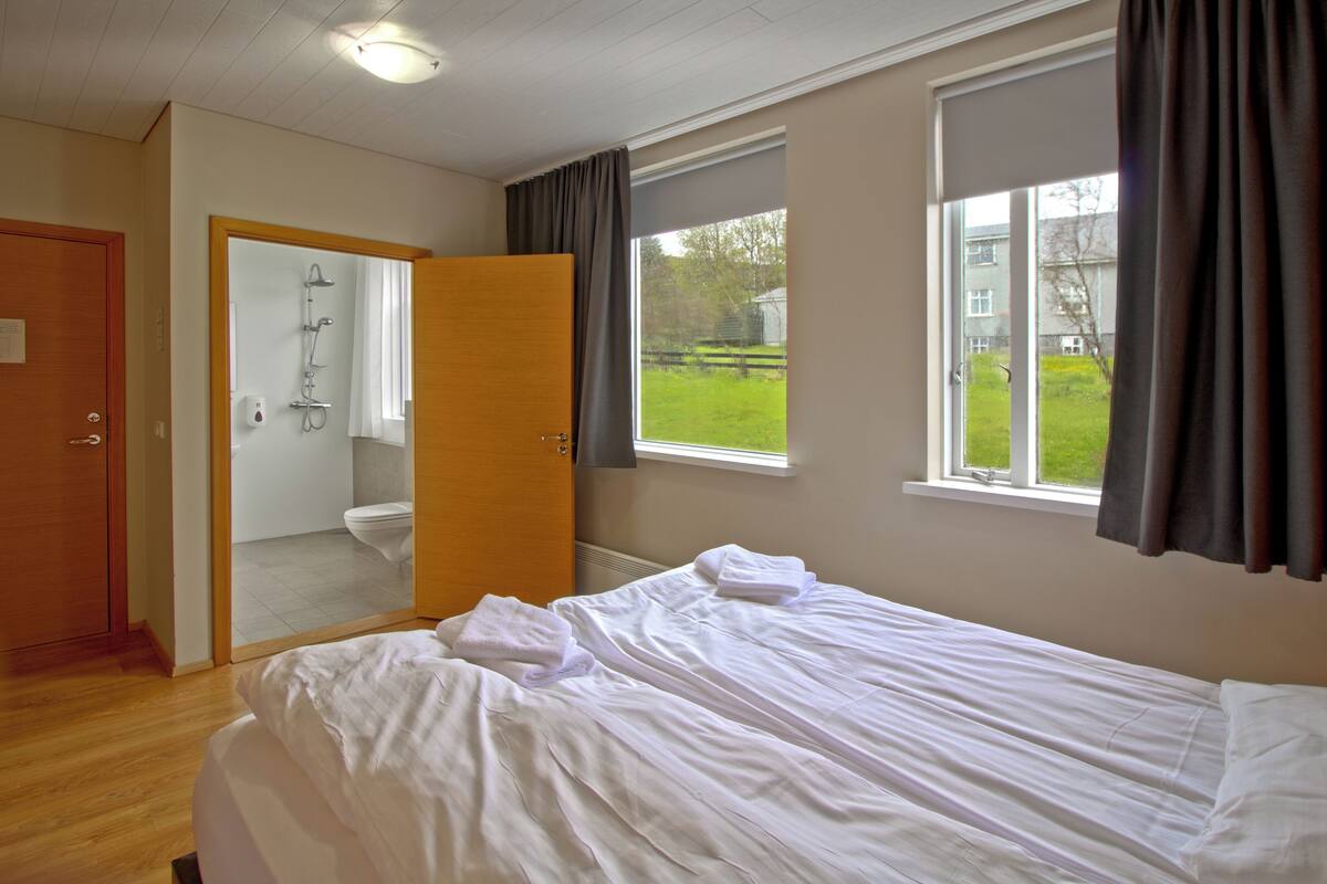 A bedroom with a bed, a bathroom with a shower, and a view of the outside.