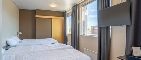 Habitación de hotel con dos camas, un televisor de pantalla plana montado en la pared y una ventana con cortinas.