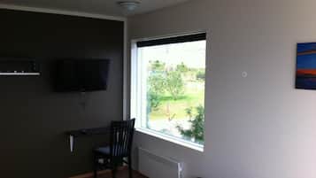 Una habitación con un ventanal grande, una silla, un televisor montado en la pared y un radiador.