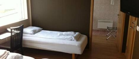 Una cama individual con estructura de madera, una pequeña silla y un televisor sobre un mueble de madera.
