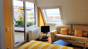 A room with a sofa, a television, and a window overlooking buildings. - Apartment Seeblick (Meersburg)
