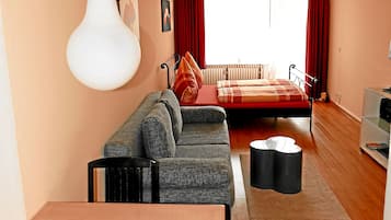 A cozy living room with a sofa, a dining table, and a bed with red curtains.