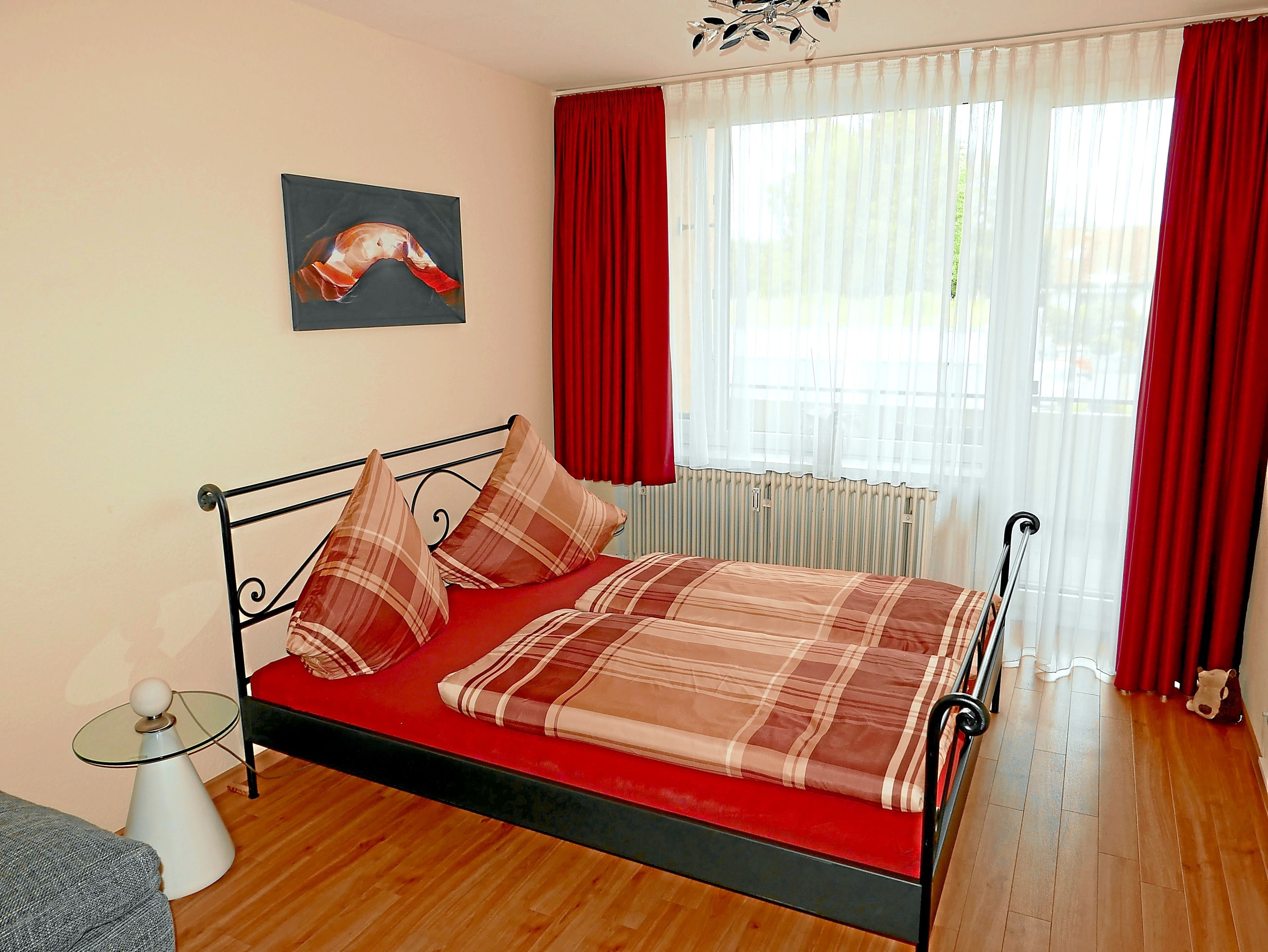 Ein Bett mit kariertem Überwurf, roten Vorhängen und einem Wandbild.