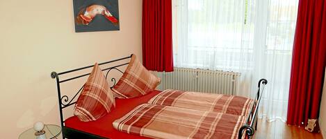 Ein Bett mit kariertem Überwurf, roten Vorhängen und einem Wandbild.