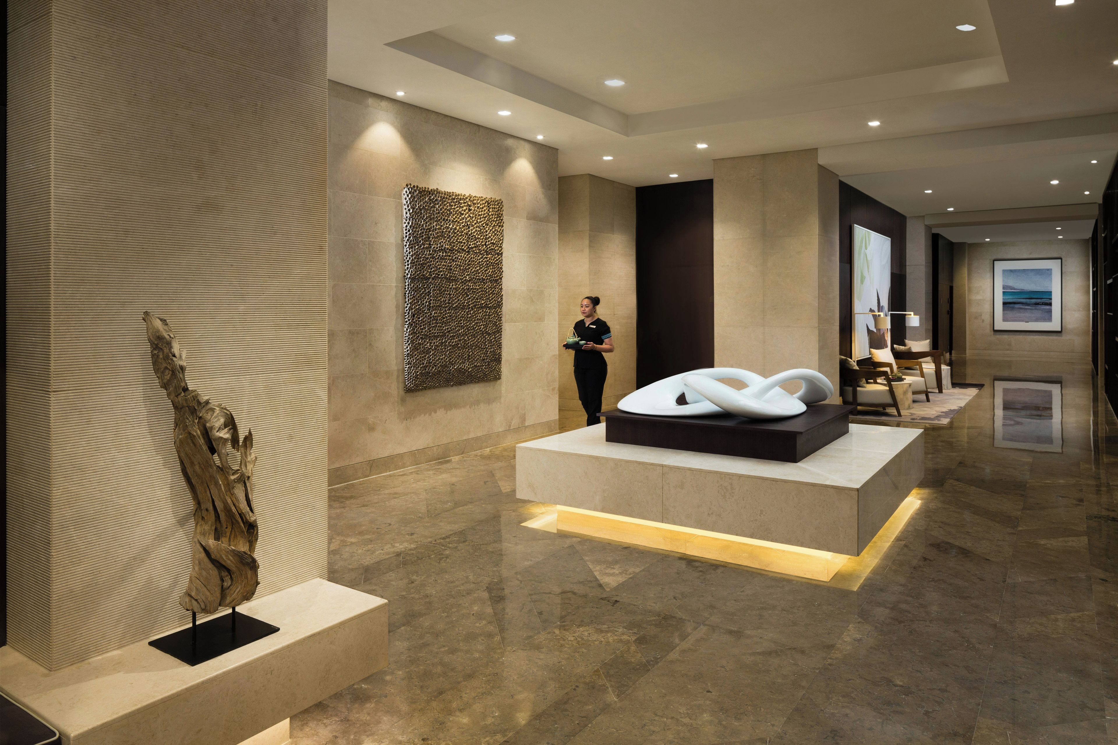 A modern lobby with a reception desk, a large abstract wall art, and a seating area with a view of the lobby.
