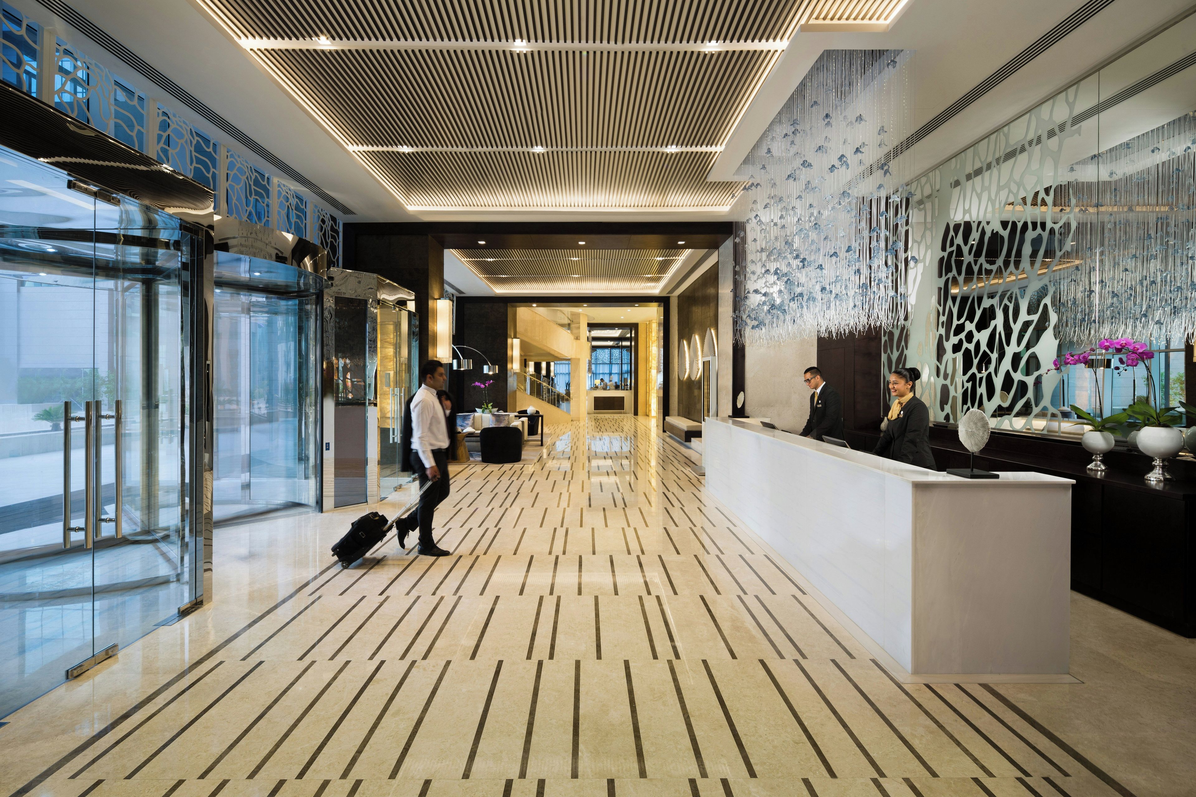 A hotel lobby with a reception desk, a glass elevator, and a patterned floor.