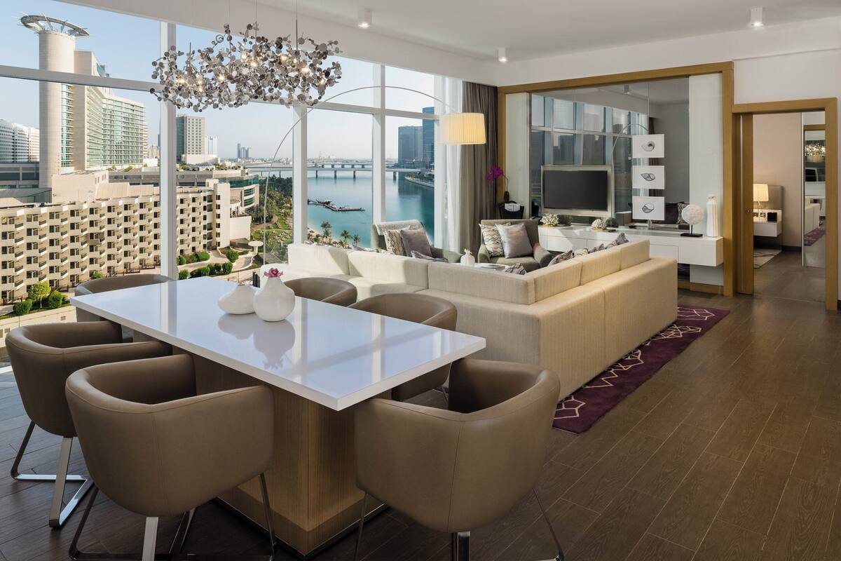 A modern living room with a dining area, large windows, and a view of a cityscape.