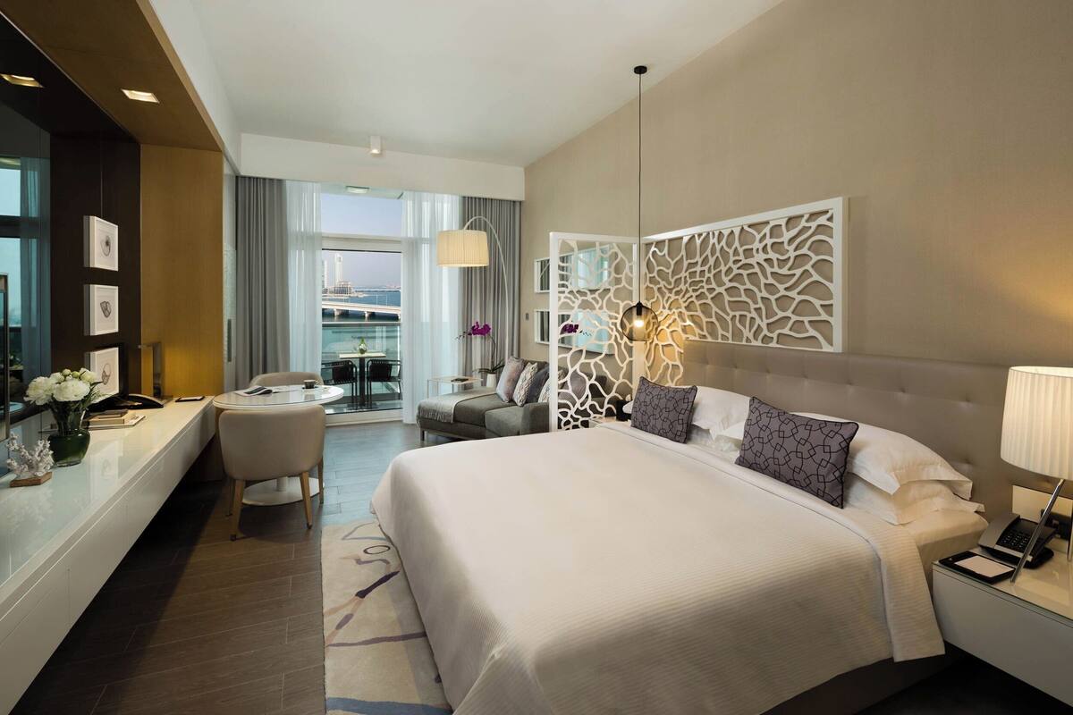 A modern hotel room with a large bed, a desk, and a view of the cityscape.