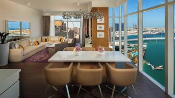 A modern living room with a dining area, large windows, and a view of a cityscape and water.