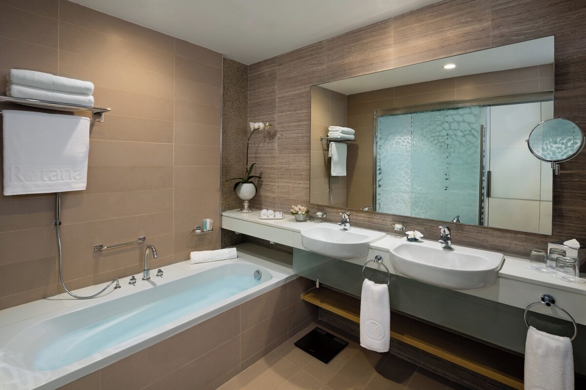 A modern bathroom with a bathtub, two sinks, and a large mirror.