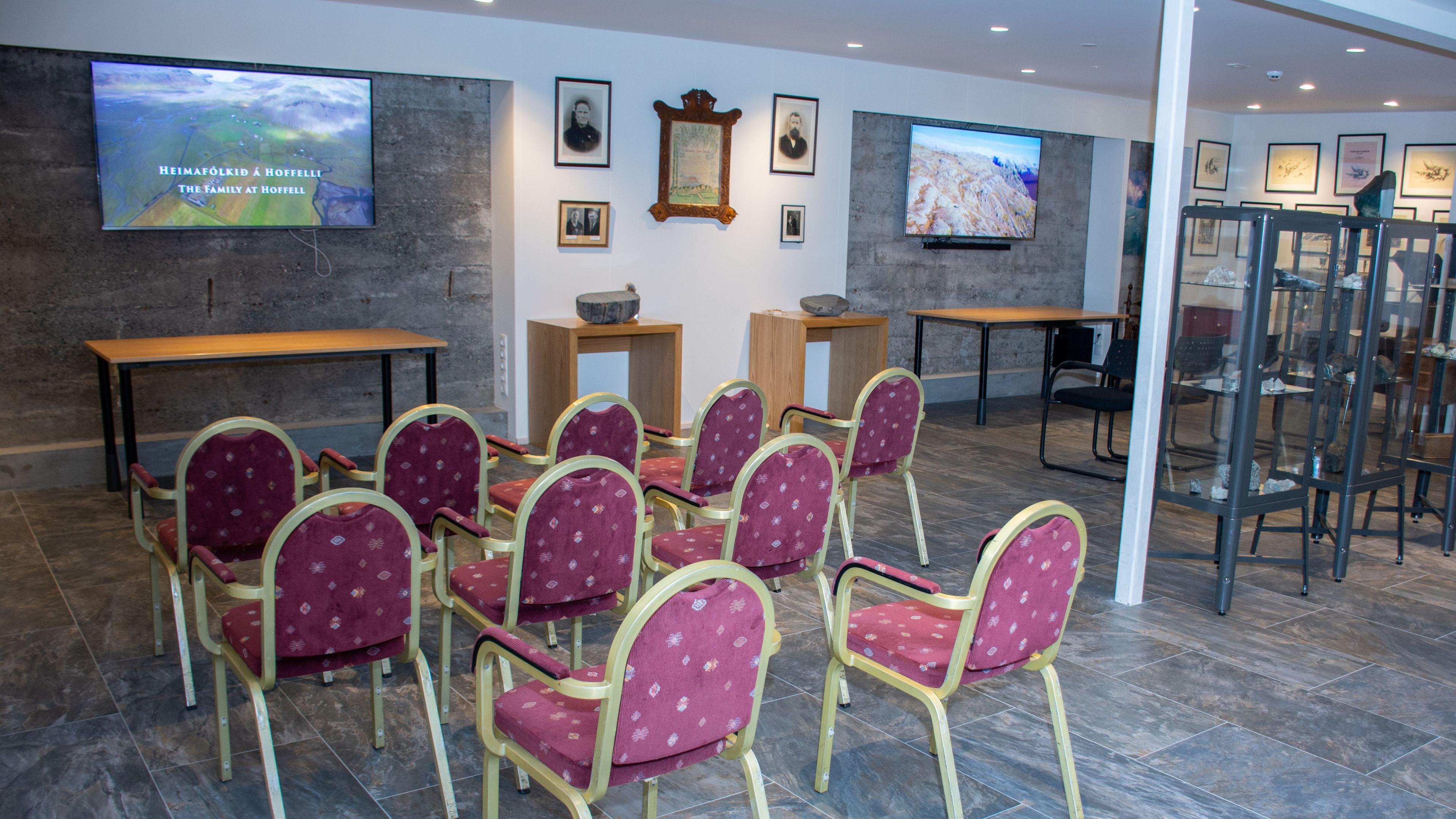 Une salle de conférence dotée d’un grand écran affichant une image de paysage, de plusieurs portraits encadrés accrochés au mur, et d’un aménagement composé de chaises et de tables.