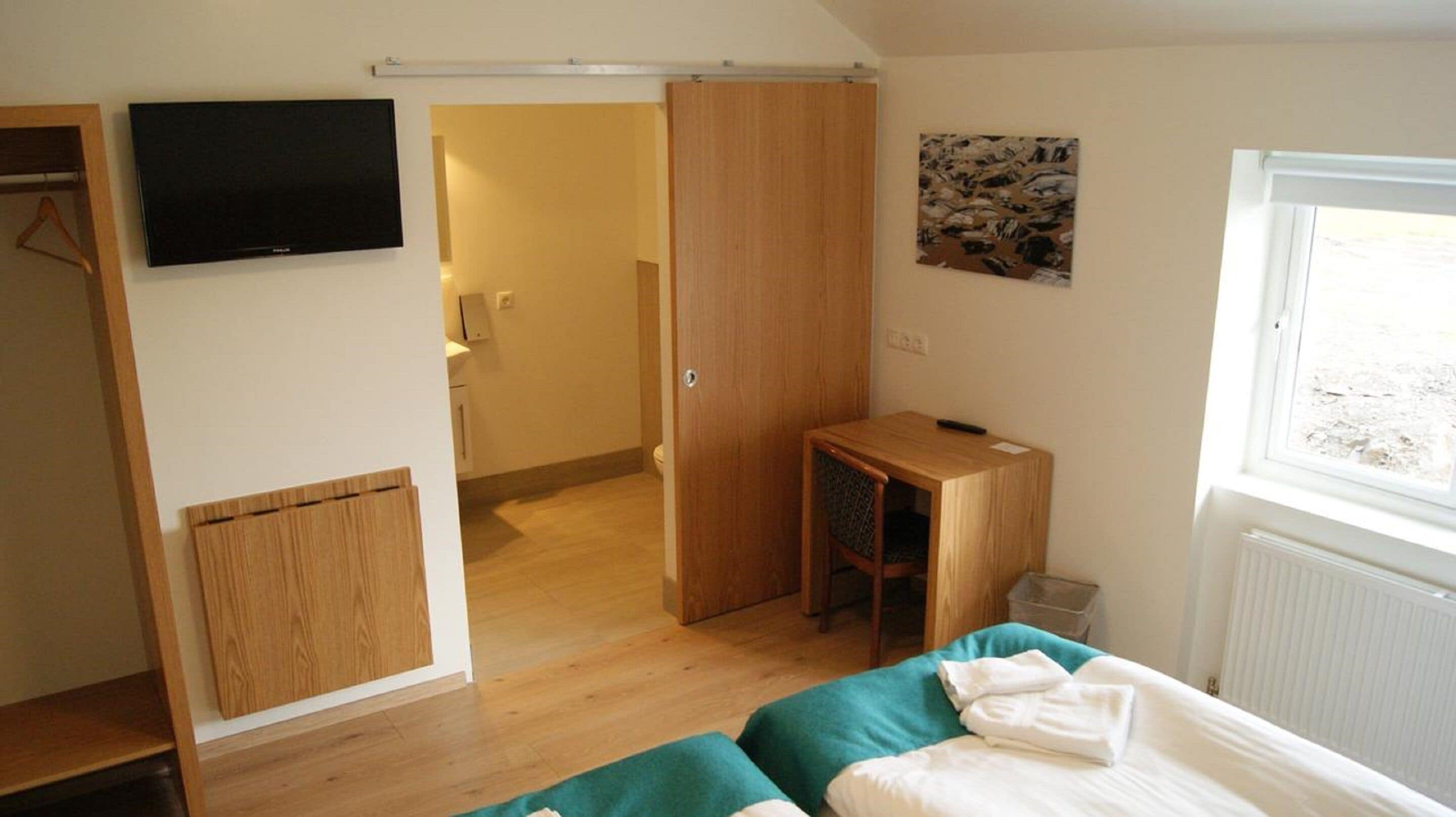 A bedroom with a bed, a desk, a television, and a bathroom door.