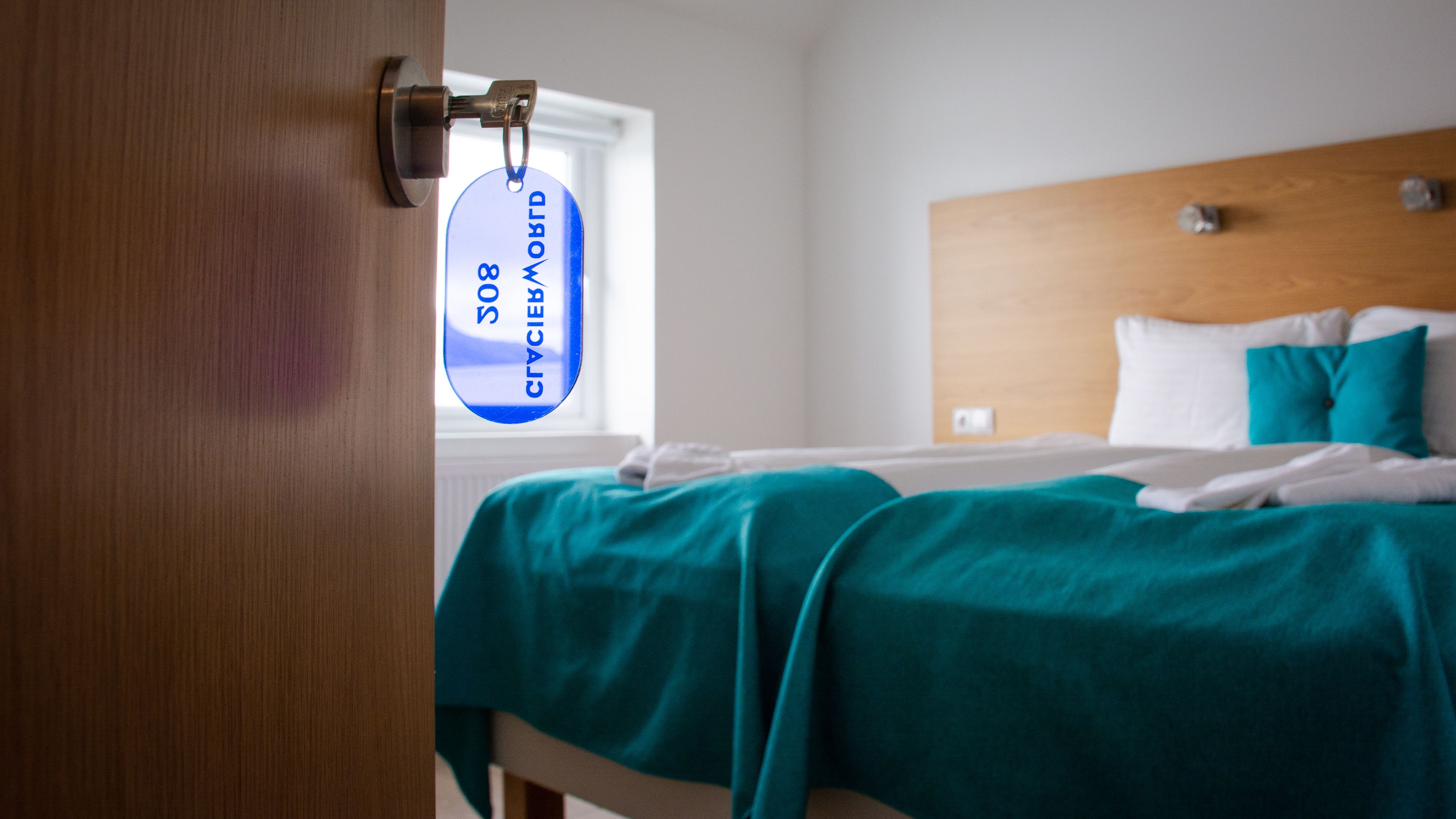 A hotel room with a bed, a window, and a door with a keycard lock.