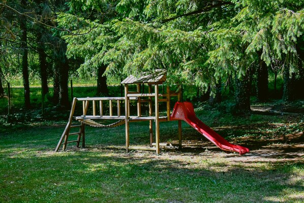 A wooden play structure with a slide in a grassy park area.