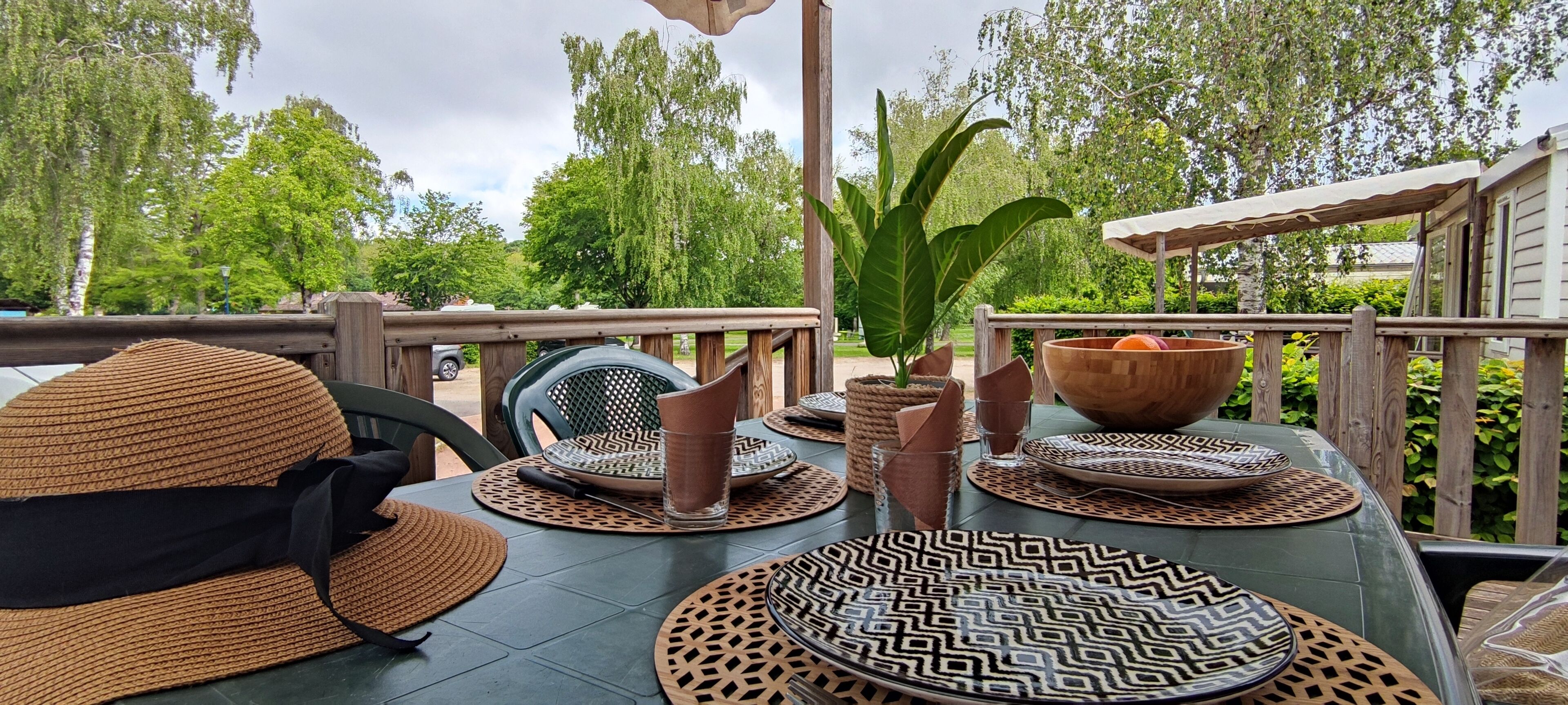An outdoor dining area with a table set for two, featuring patterned placemats and a woven basket.