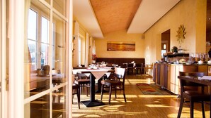 A spacious dining area with wooden flooring, large windows, and a central table with chairs.