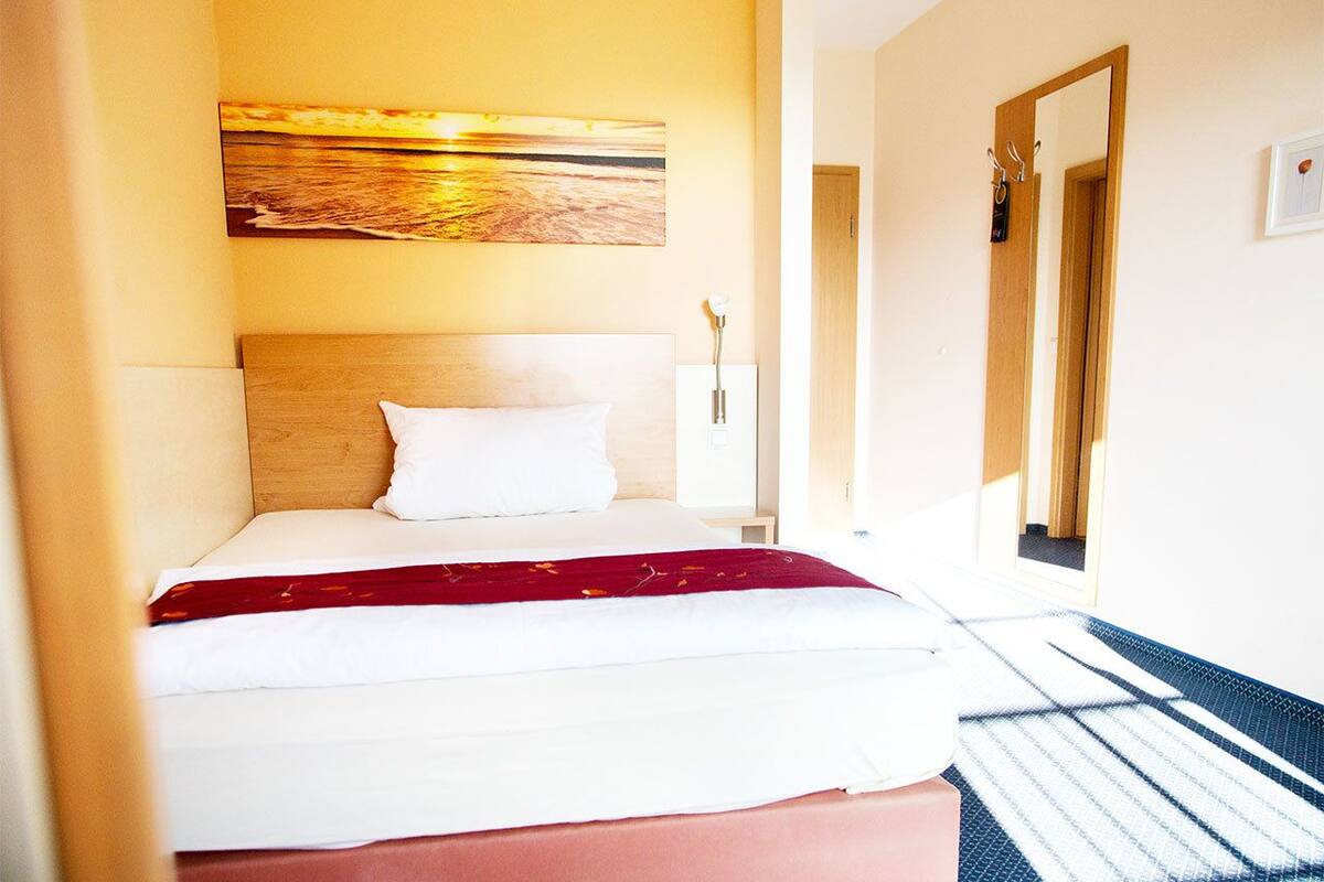 Una habitación de hotel con una cama, un cuadro sobre la cama, una mesita de noche y un espejo.