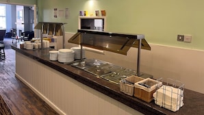 A buffet setup with a counter, stacked plates, and a variety of food items. - Fairhaven Hotel Central Blackpool (Blackpool)